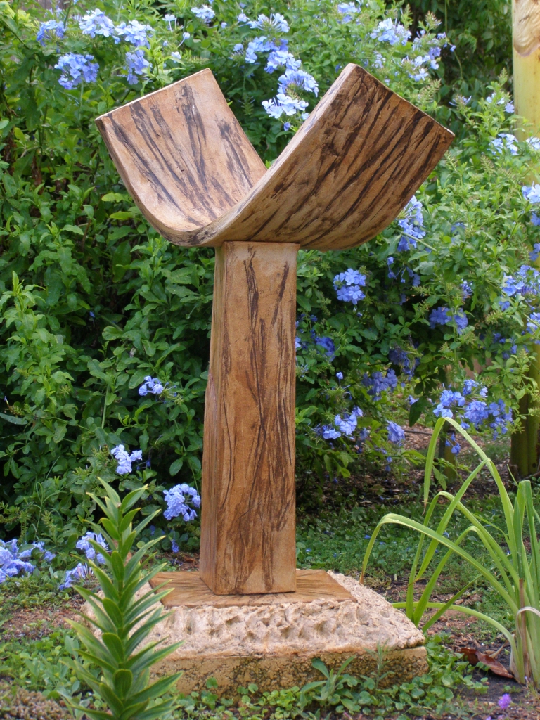 wood sculpture in yard with flowers in background