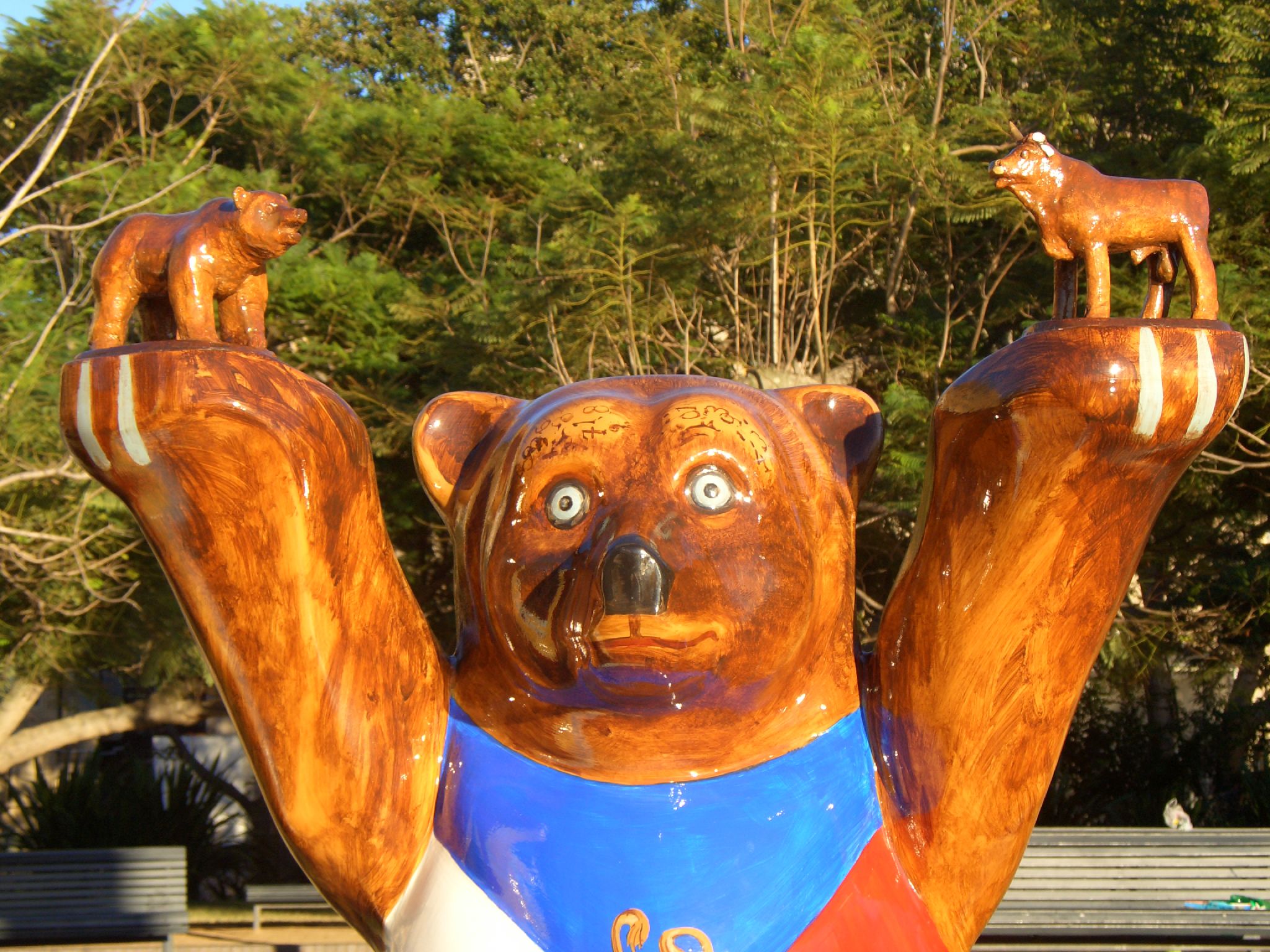 the bear statue is made of wooden with blue bibs and holds his hands up in the air