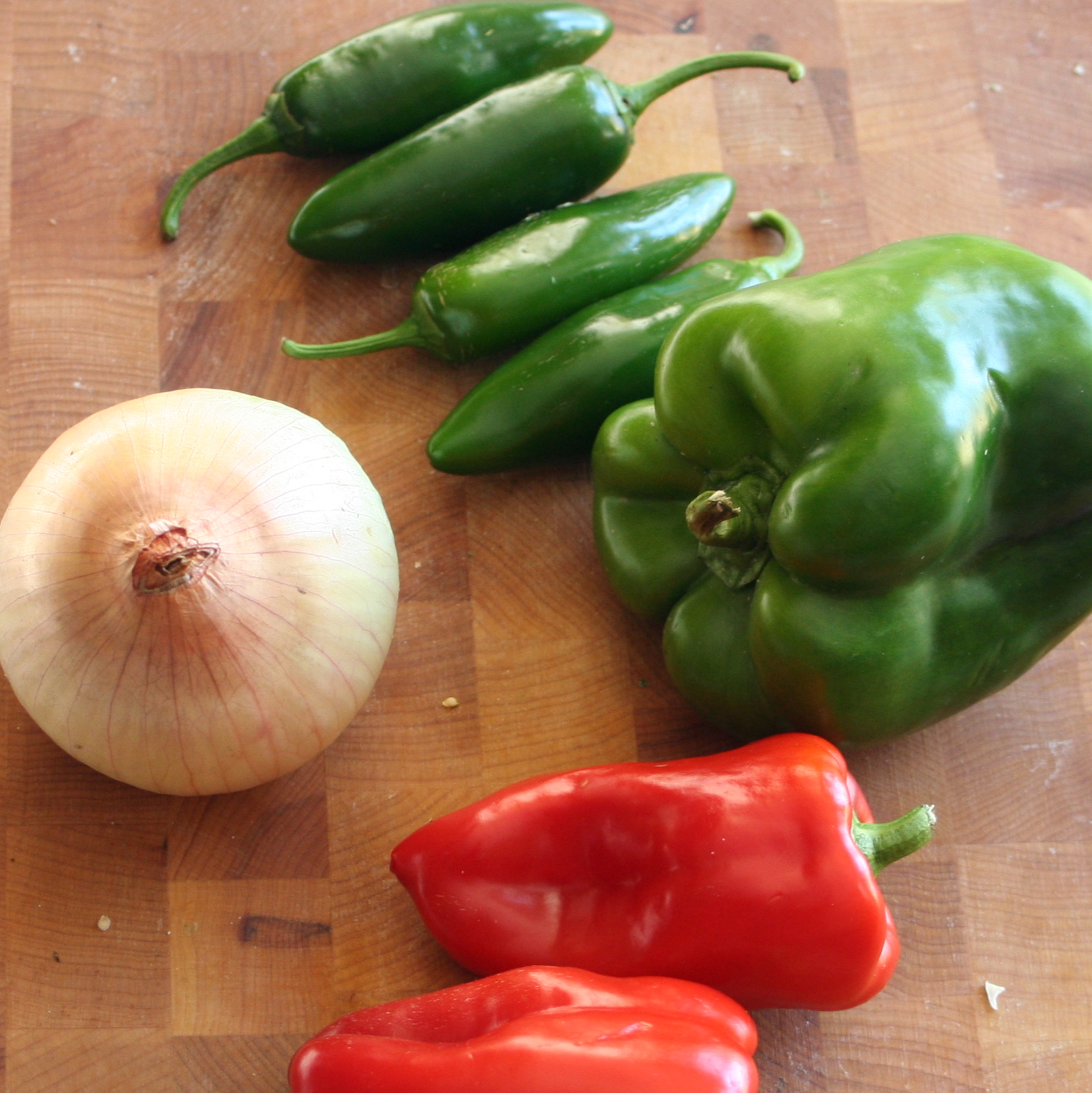 some red peppers, green peppers, and a garlic on a wooden  board