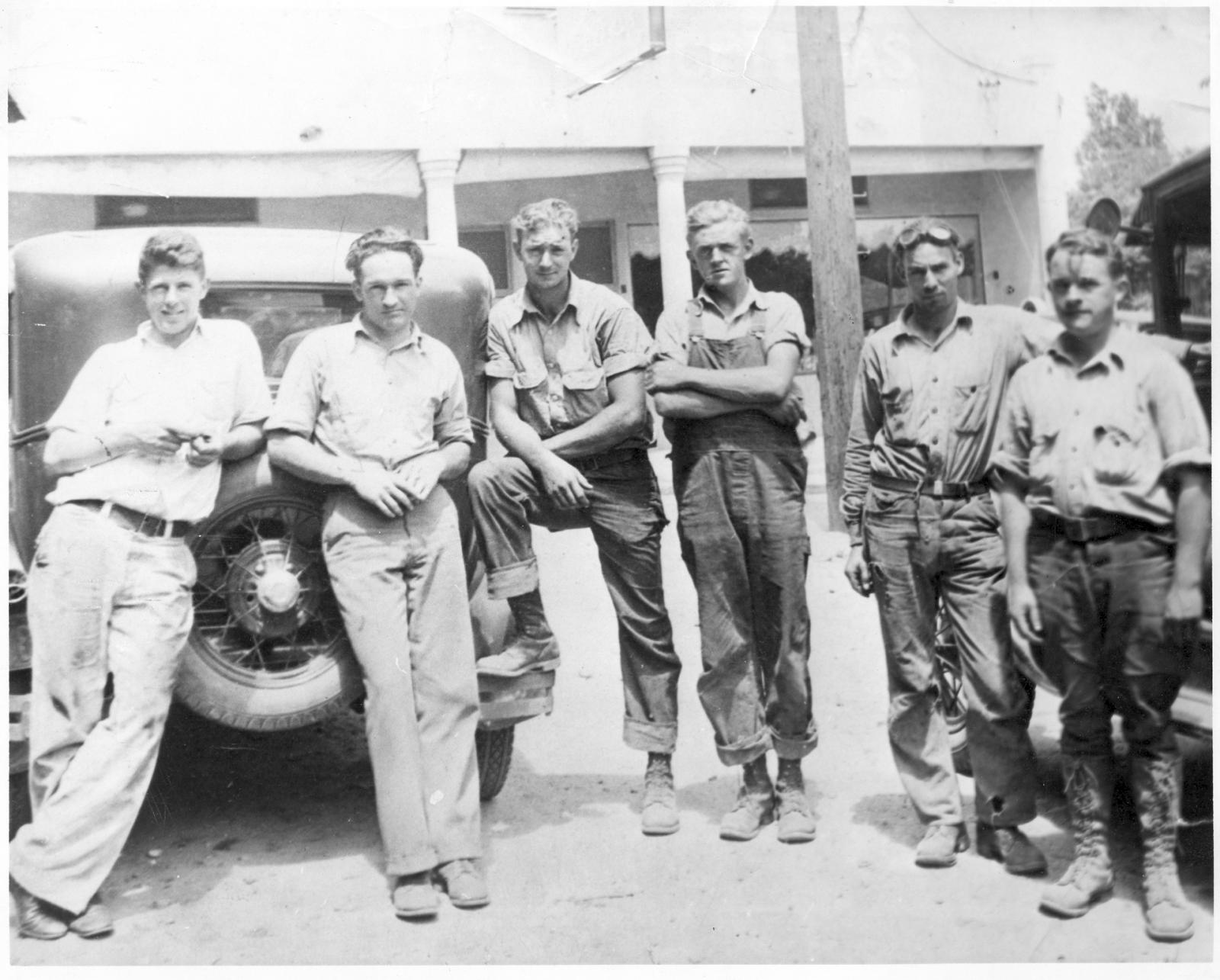 black and white image of five men standing in front of a truck