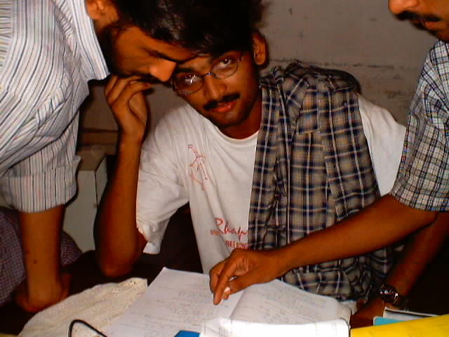 the two men are looking at a paper while one man with glasses looks on