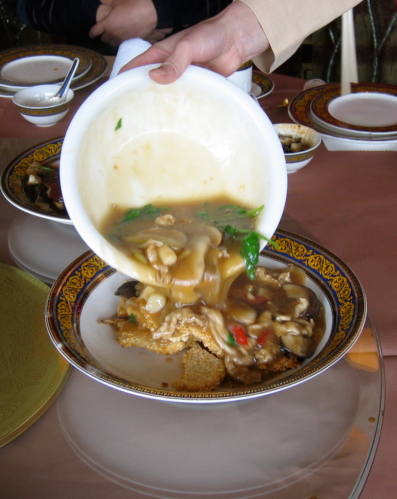 someone pouring broth into a bowl filled with different dishes