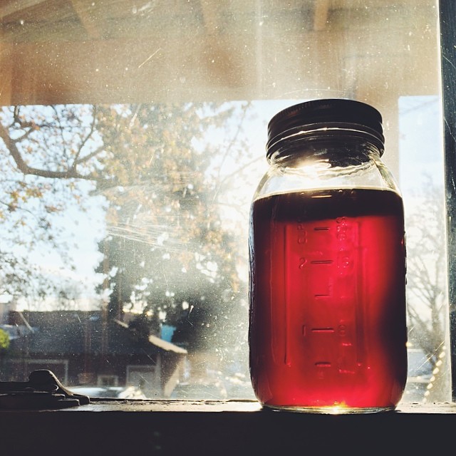 a jar with a red liquid on top is next to a window
