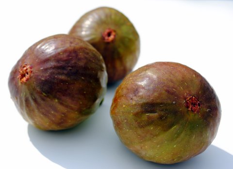 three green, aged figs sitting on top of a table