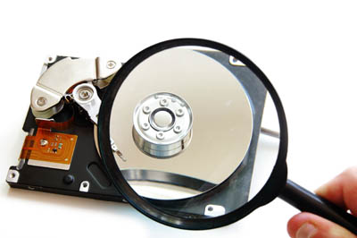 a hand holding a magnifying glass up to a hard drive