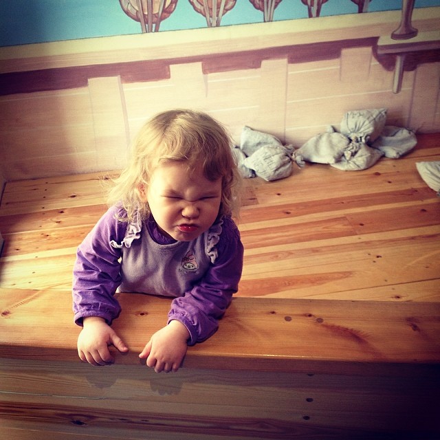 a little girl standing on a wooden bed
