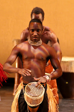 men are performing in the street and one holds a drum