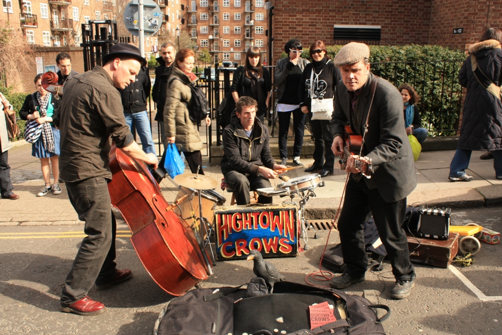 musicians play music as people watch from the sidewalk