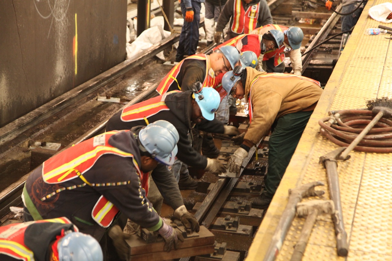 many people wearing helmets work together on a train track