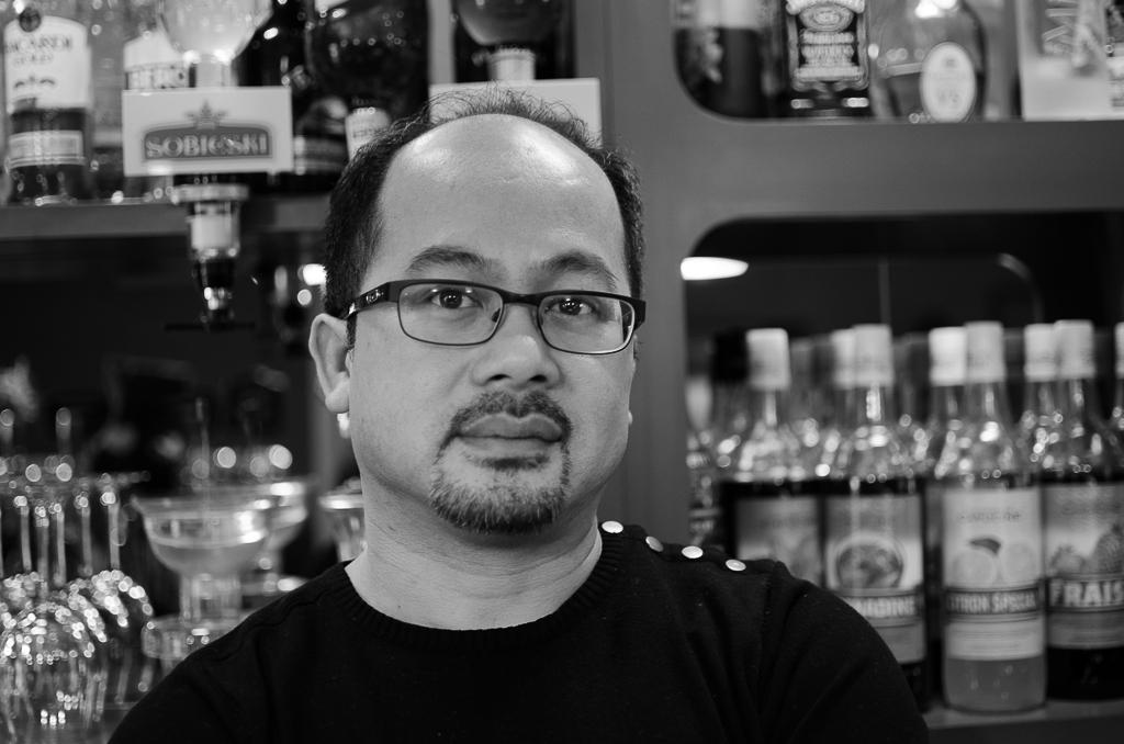 a man wearing glasses standing by wine glasses