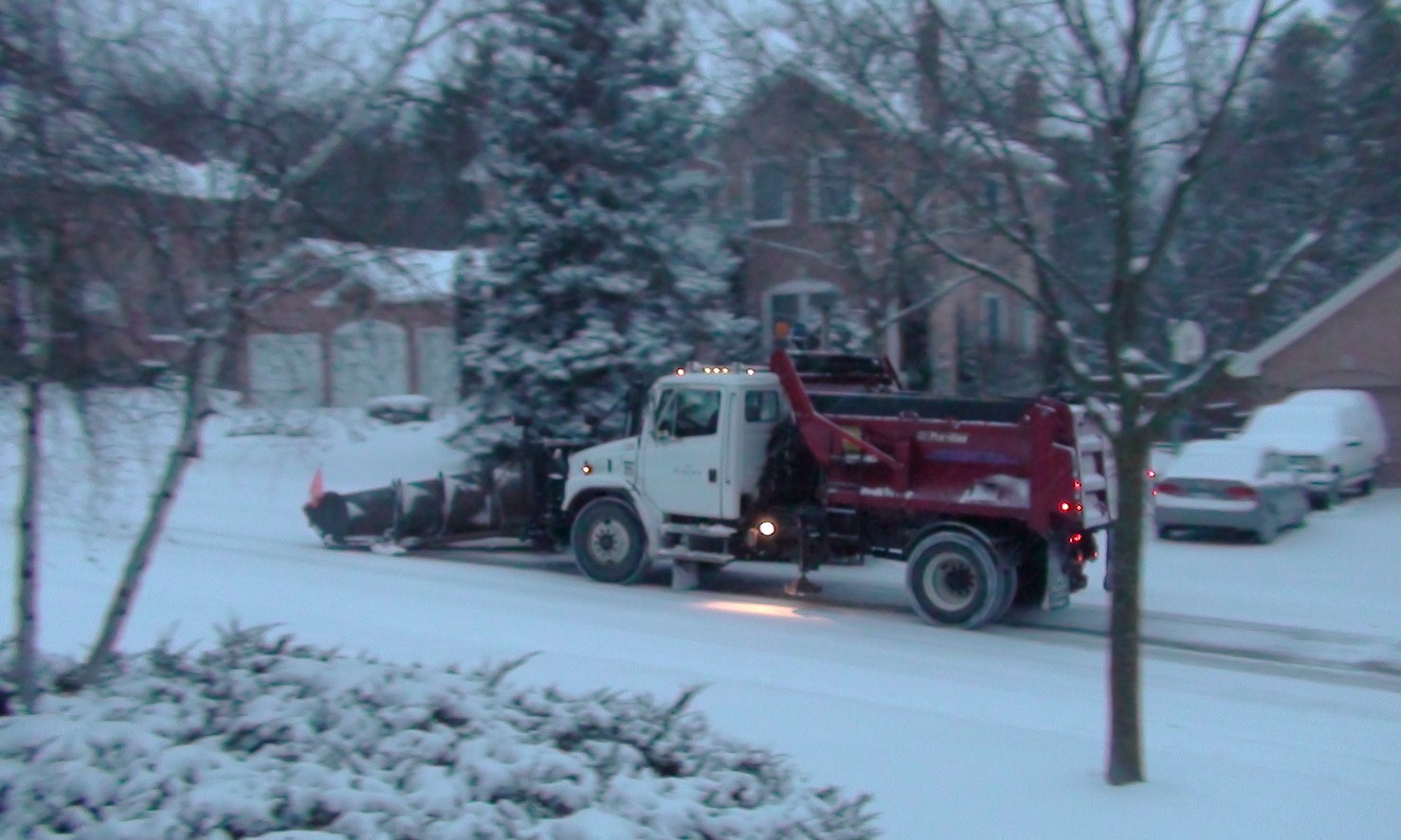 a red tow truck on snowy street next to houses