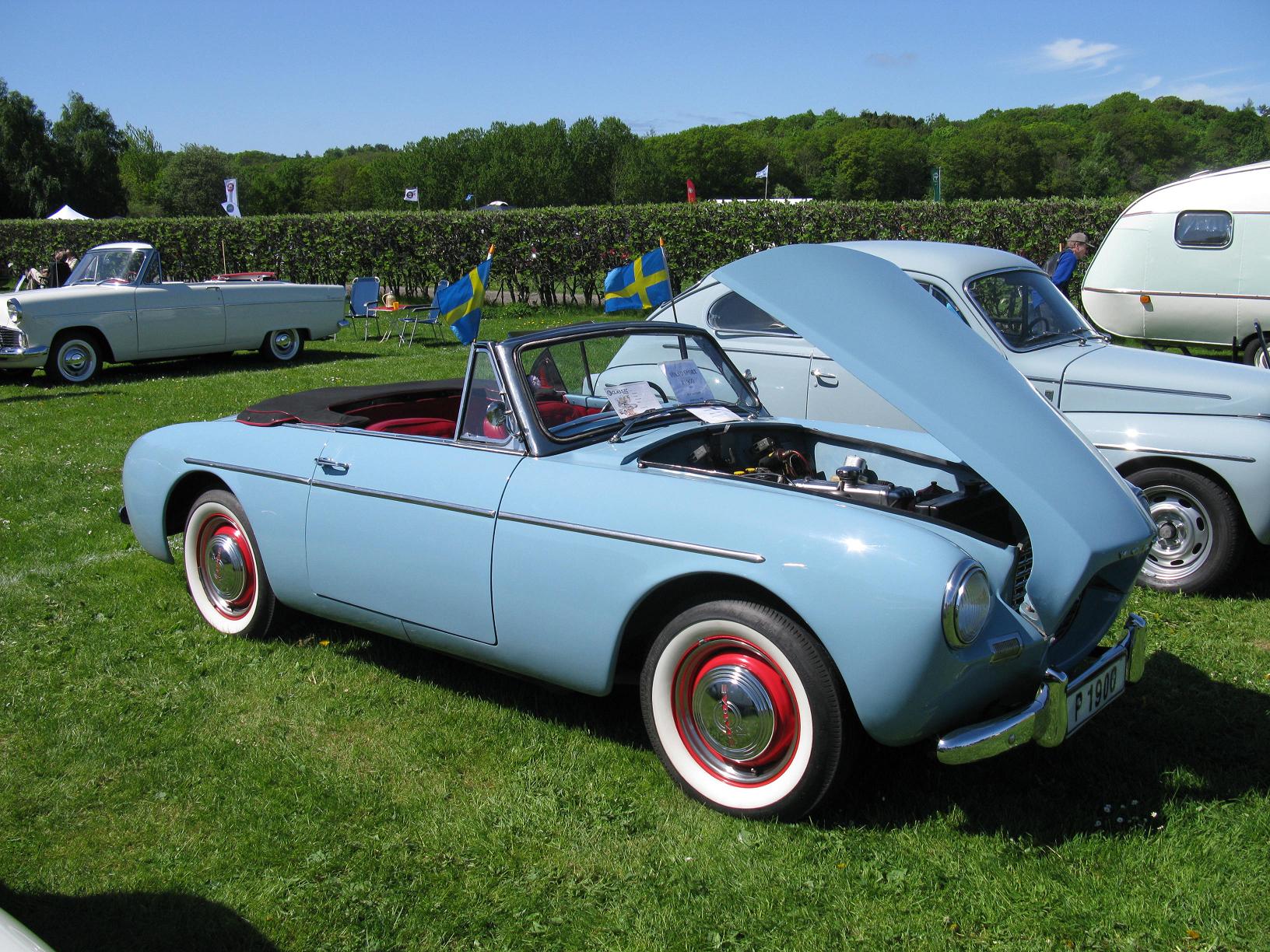 a blue convertible parked in a grassy field next to other cars