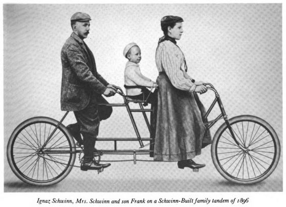 the man is standing beside a woman, while a young child sits on a tiny bike