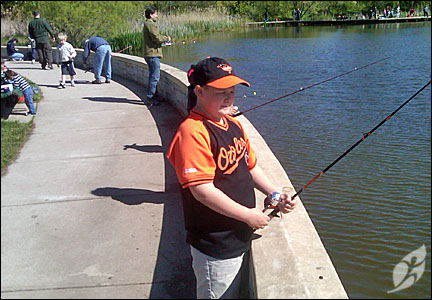 a man in orange shirt standing by a body of water with fish on rod