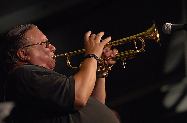 a man wearing glasses holding a trumpet and playing the trumpet