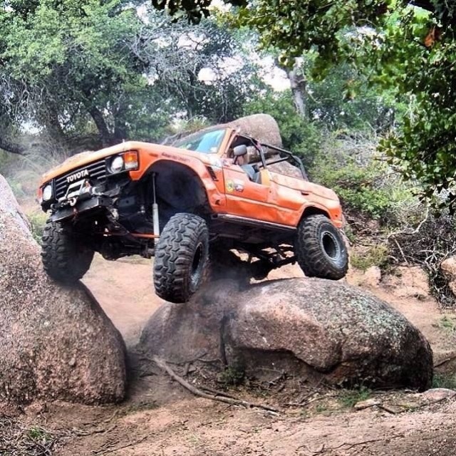 an orange truck jumping over rocks with trees in the background