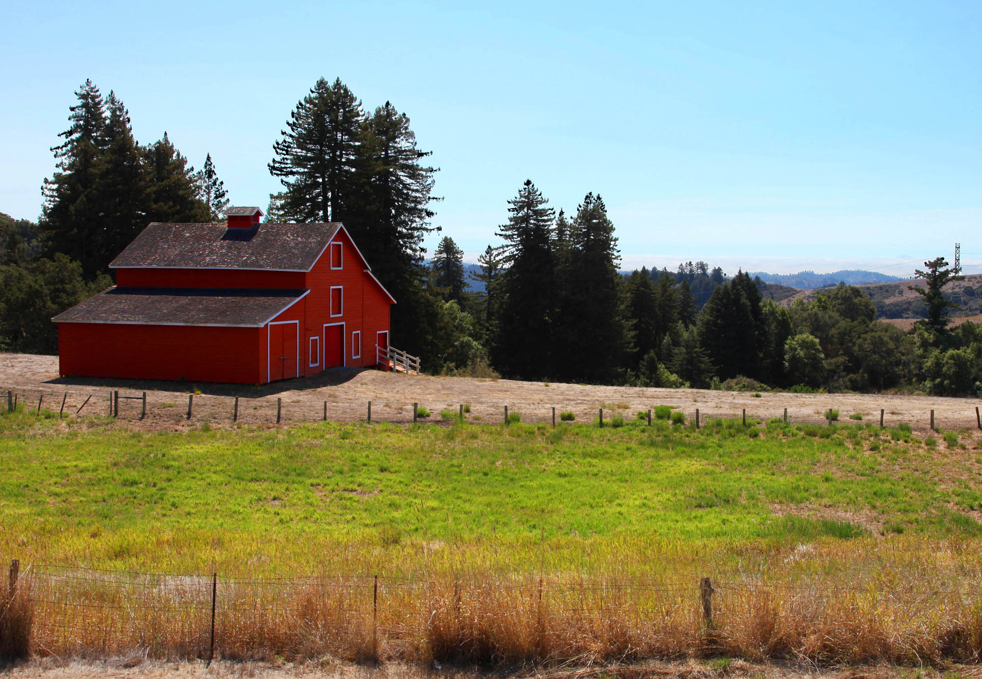 a barn with a red building sits next to a fence and tall trees