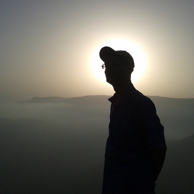the sun setting over mountains with a man standing at sunset