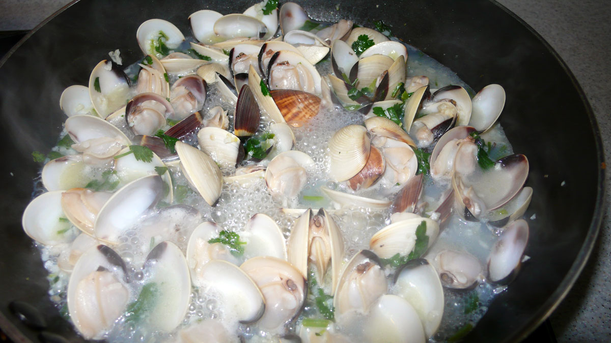 a wok filled with clams and broccoli cooking on the stove