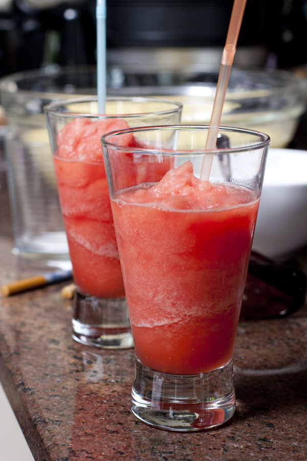 three glasses filled with red liquid and some spoons in the background