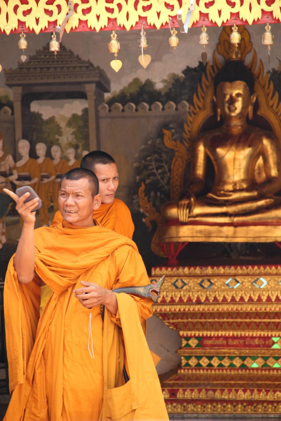 two monks standing near a statue with their cell phones in their hands