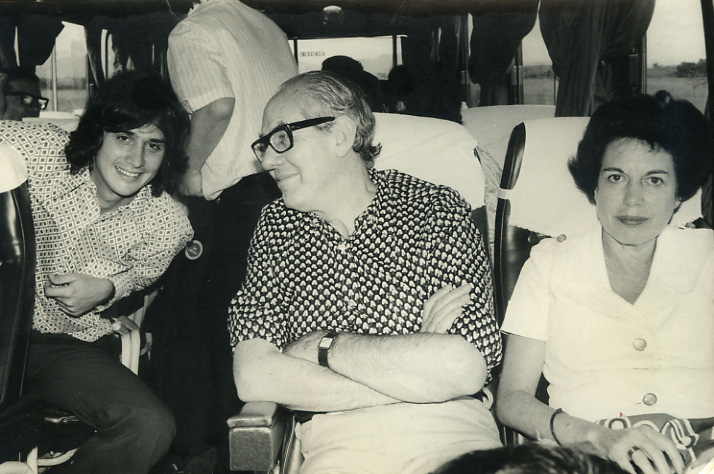 a man in a wheelchair with his arms crossed sitting on a bus next to a woman, another holding their arms out, while others look on the