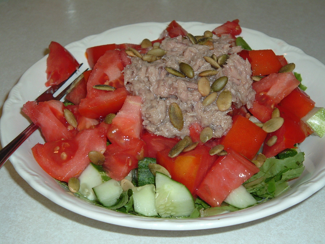 the salad has slices of watermelon, cucumber, tomatoes and seeds on it