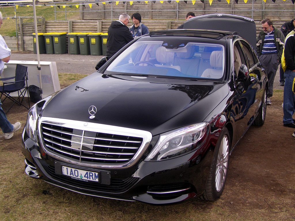 a black mercedes benz is parked next to people