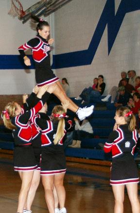 cheerleaders in black and red outfits holding cheerleader on their backs
