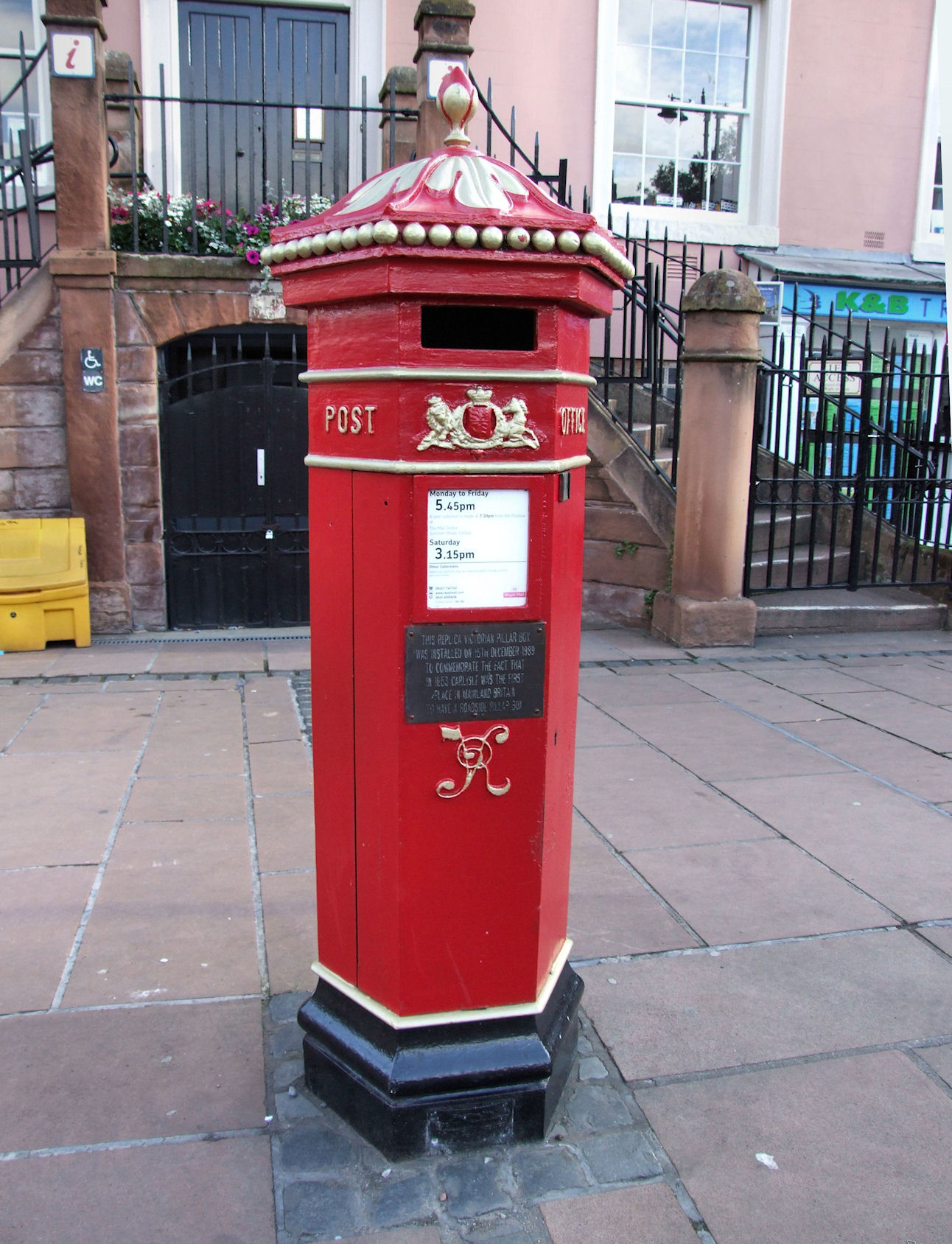 a red mailbox on a cement sidewalk near some buildings