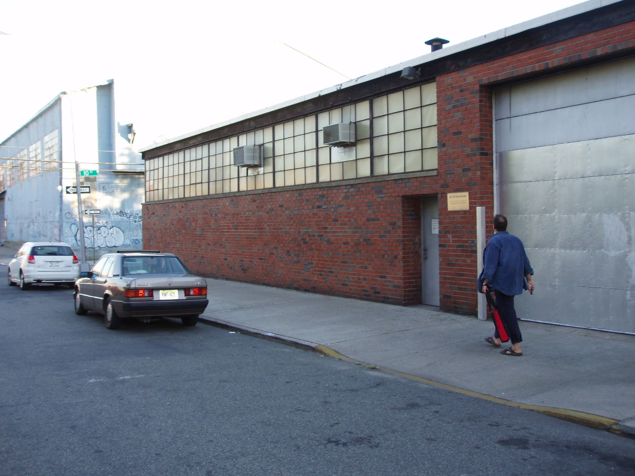 the back of an old red brick garage next to a garage with a car parked