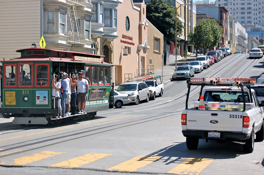 several people ride in a cable car on a city street