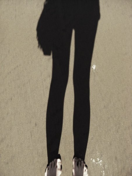 a shadow of a person wearing sandals standing in the sand