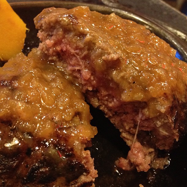 meat patties being prepared in a pan with a lemon