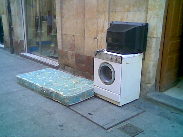a mattress, a microwave and television sitting on the side walk
