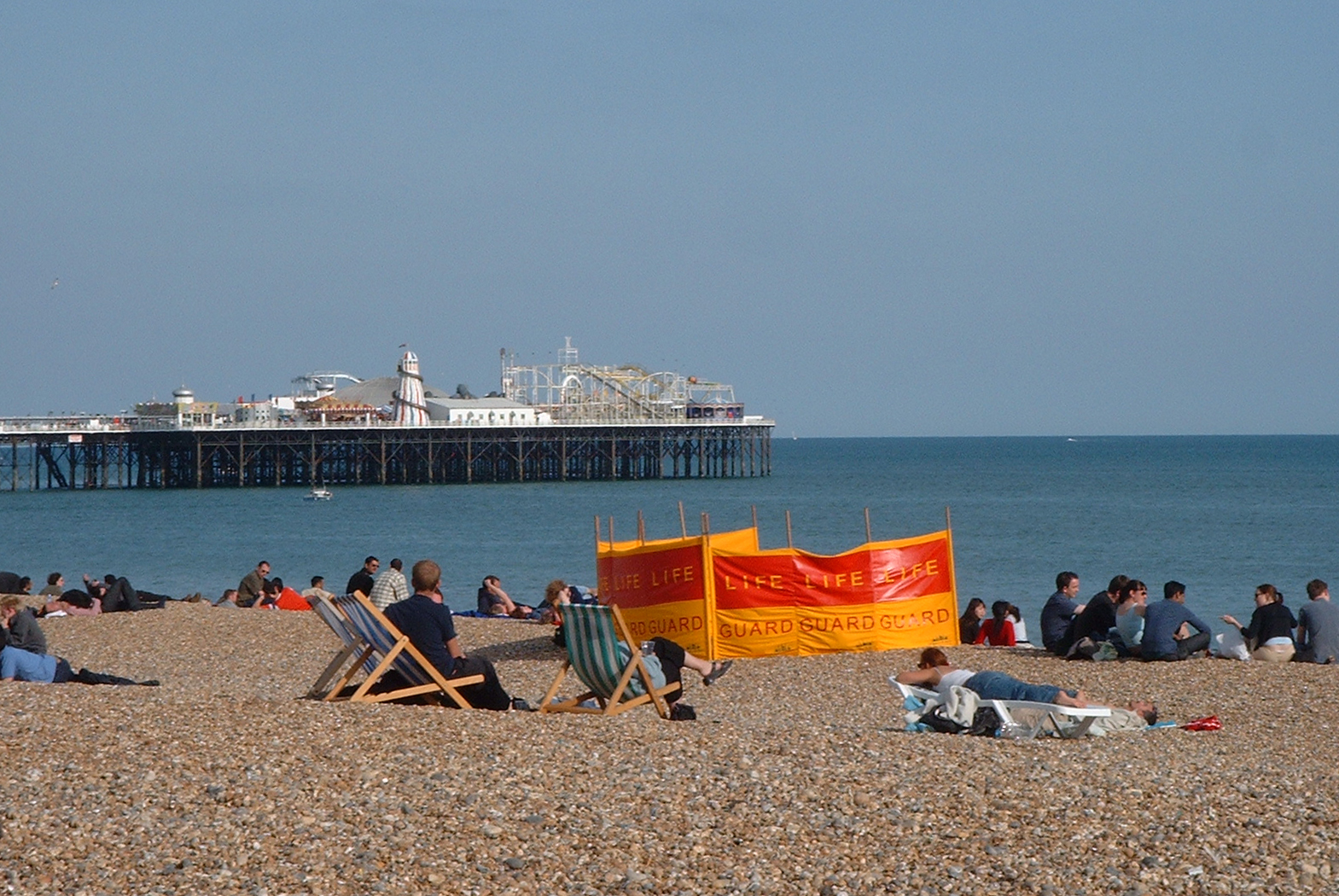 people sitting on the beach near a pier and building