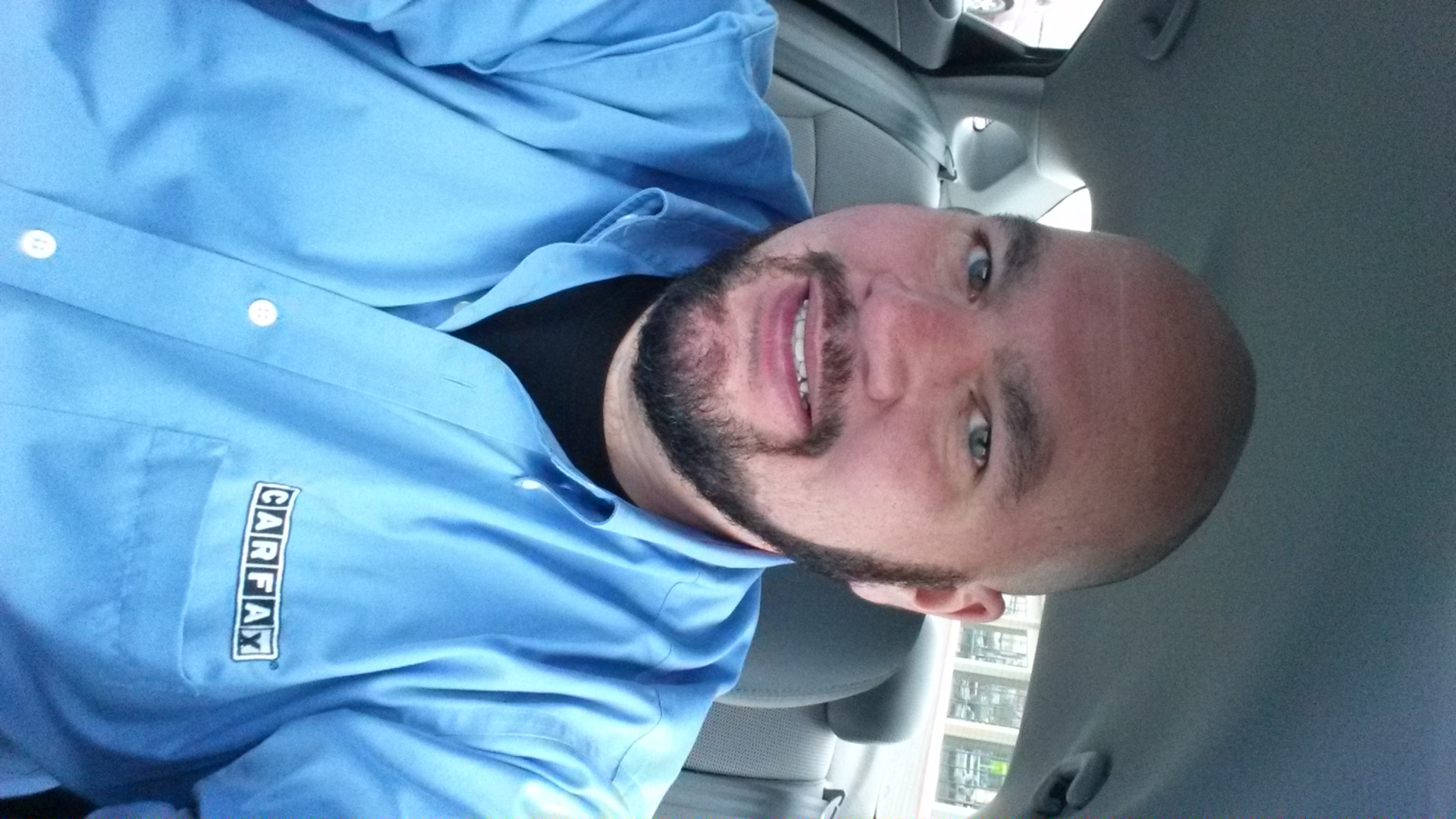 bald man in blue shirt sitting in a car