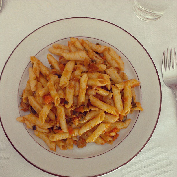 a plate of pennets, pasta, fork and spoon