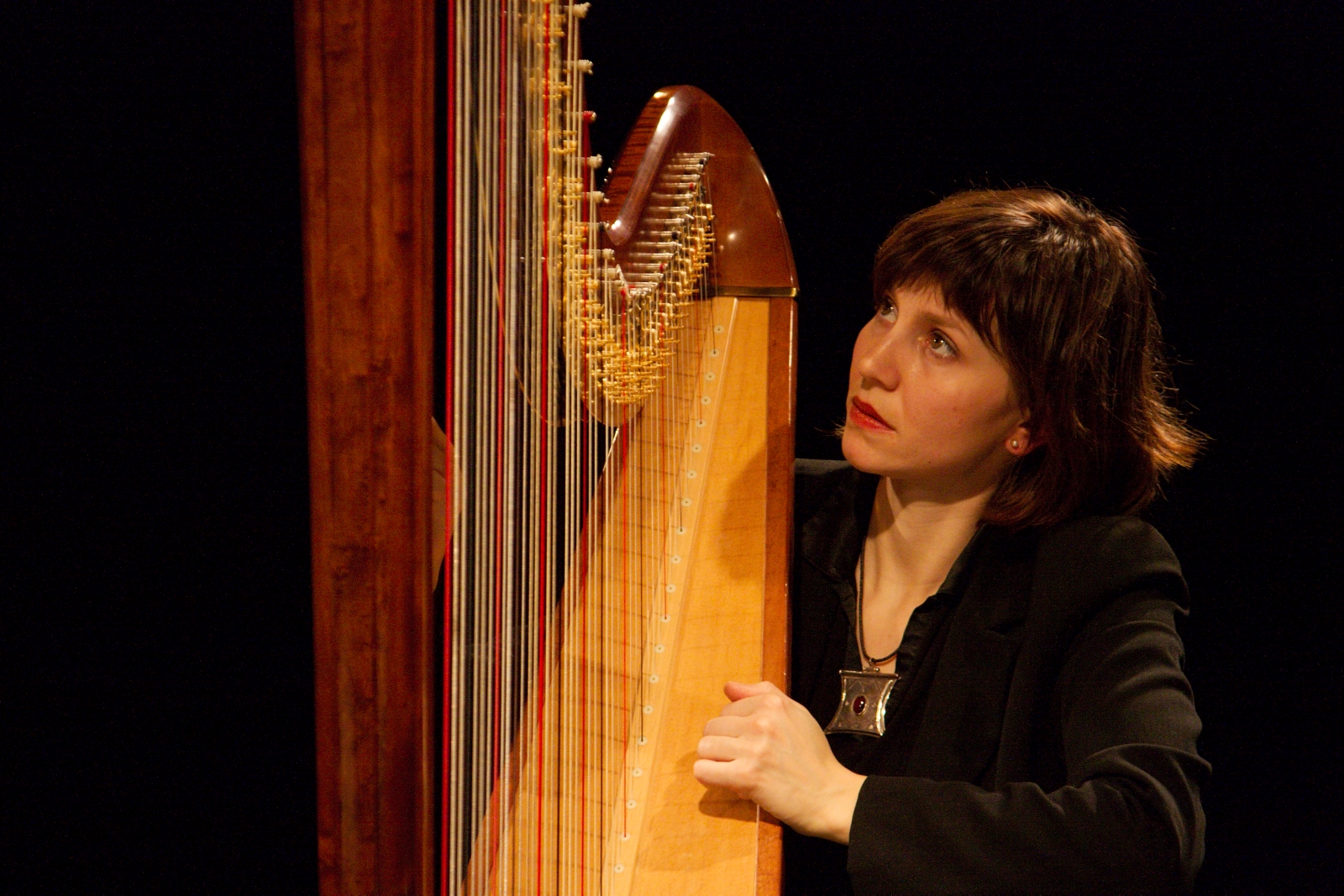 woman playing large wooden harp in dark room