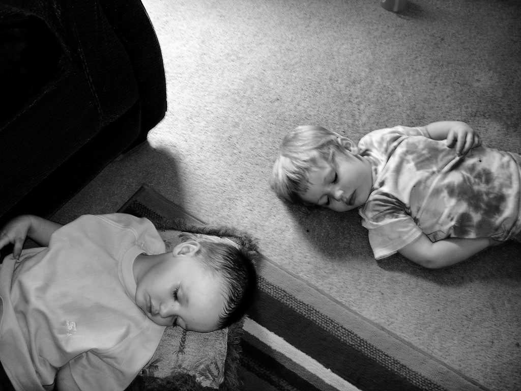 black and white pograph of two young children lying on floor next to large sofa