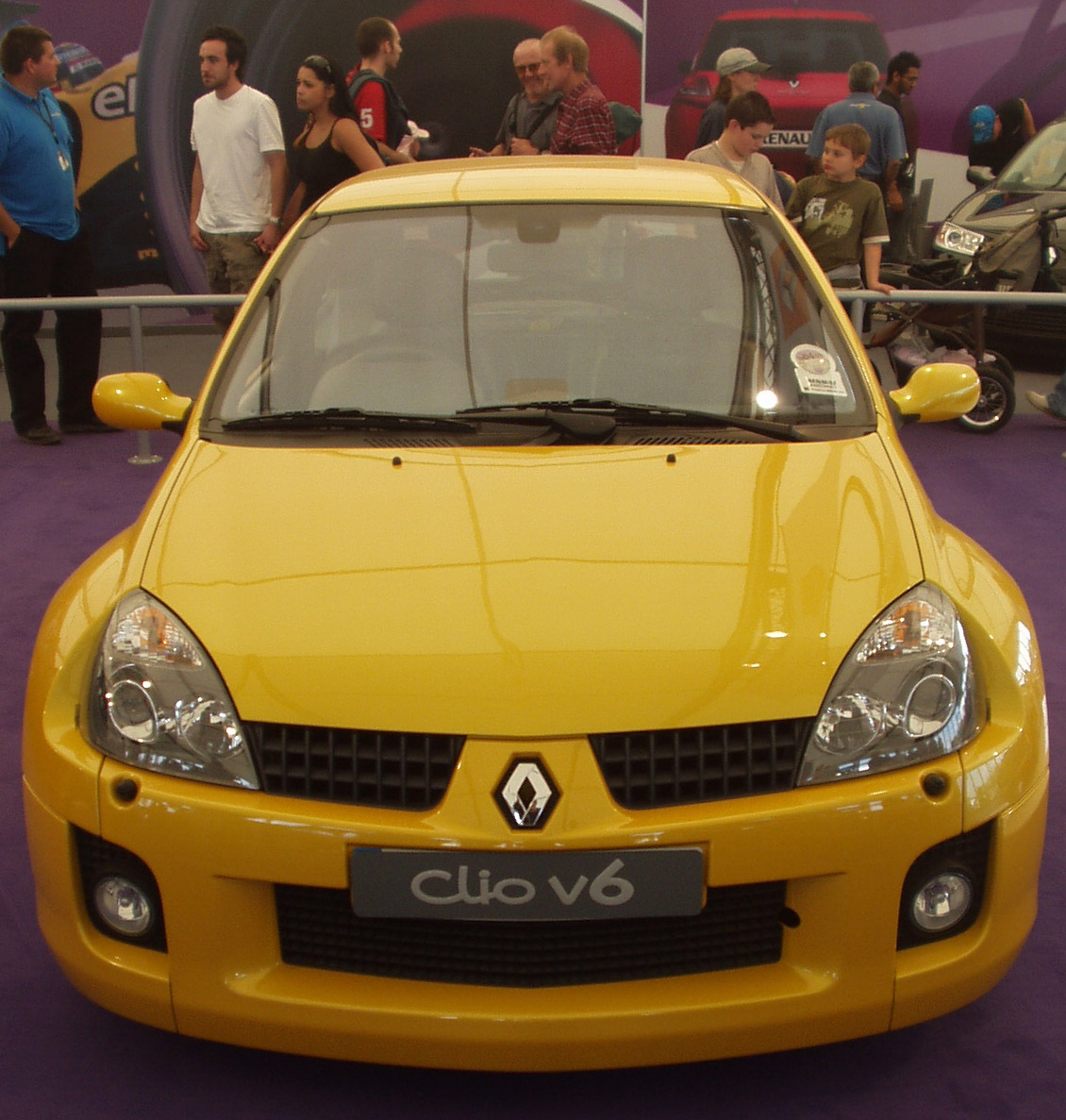 a yellow car parked on top of purple carpet next to a crowd
