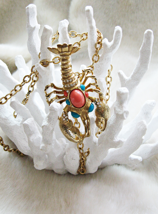 a gold necklace with dragon charms sits on a white coral