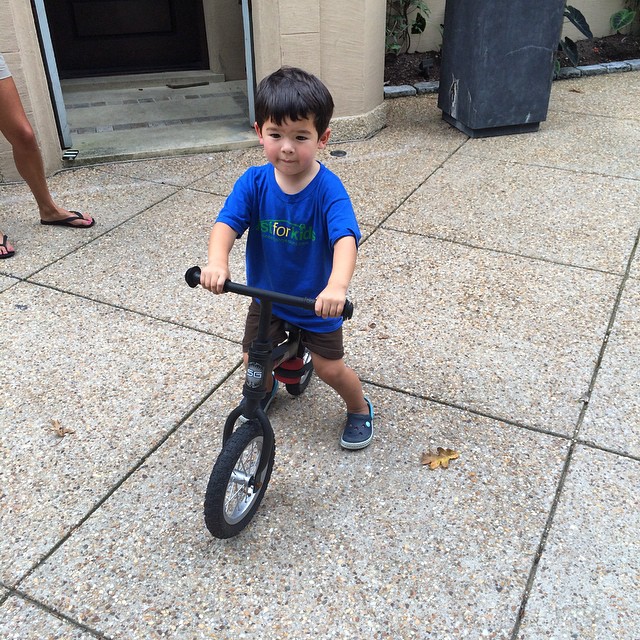 the boy smiles while riding his balance bike