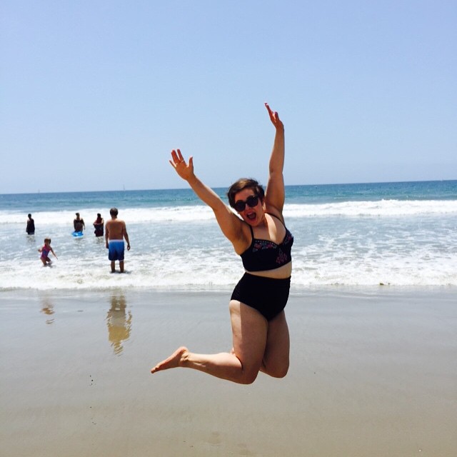 a woman wearing a black swimsuit leaping in the air while on top of a beach