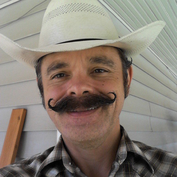 a smiling man wearing a cowboy hat and moustache