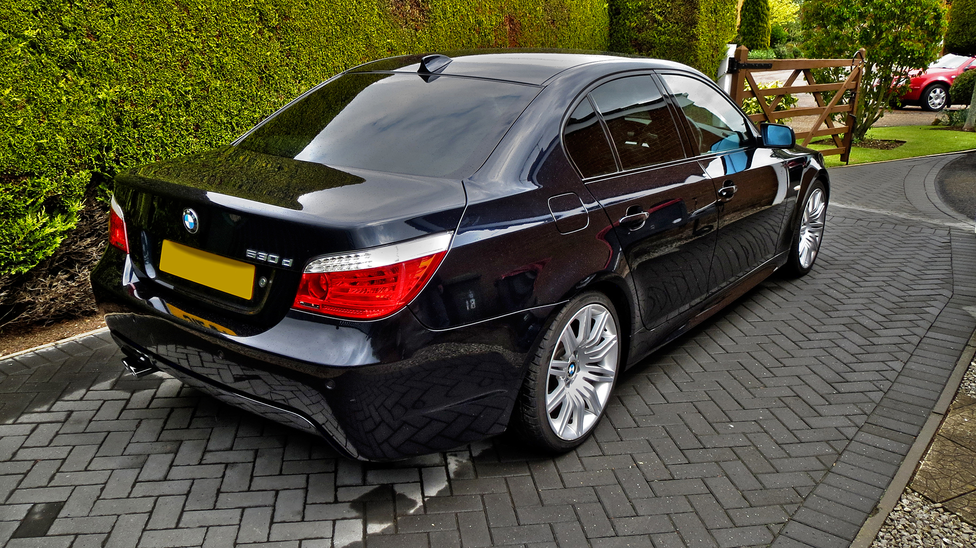 black car parked on a paved area between bushes