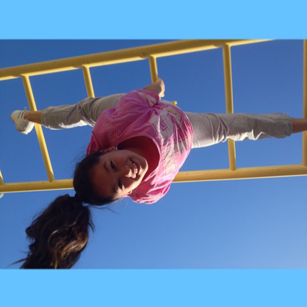 a little girl hanging upside down on the edge of a metal gate