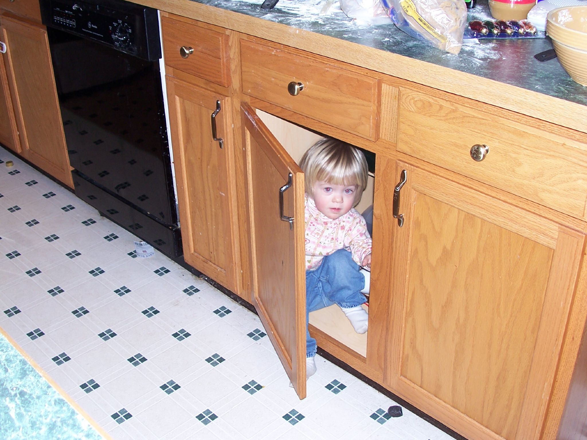 a little girl sitting in the corner of a kitchen cupboard