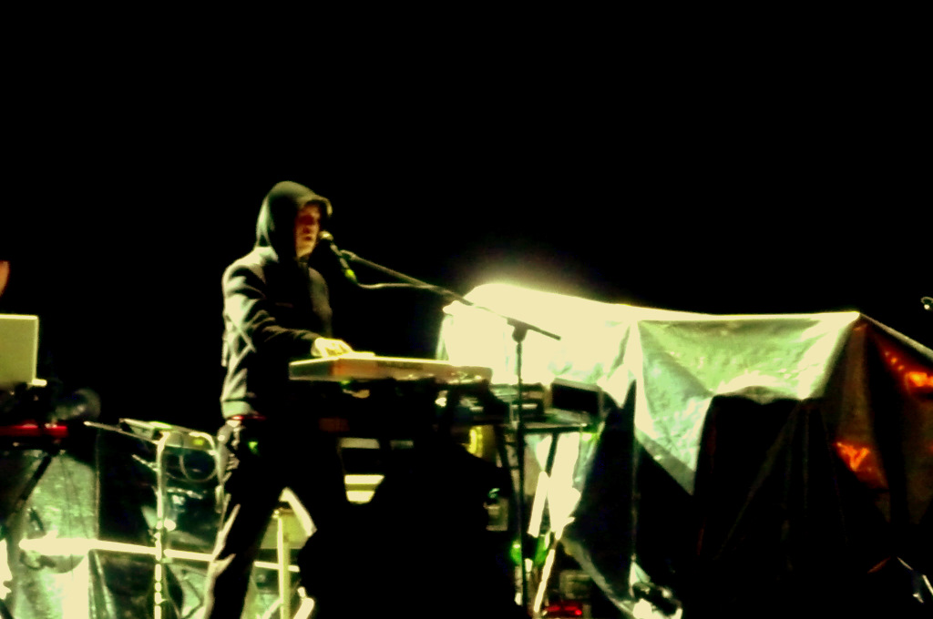 man in hooded jacket standing on stage with microphone