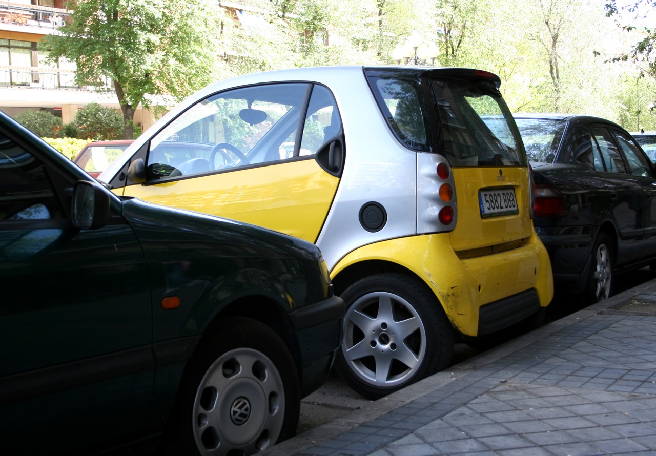 small electric cars on a street lined with parked vehicles